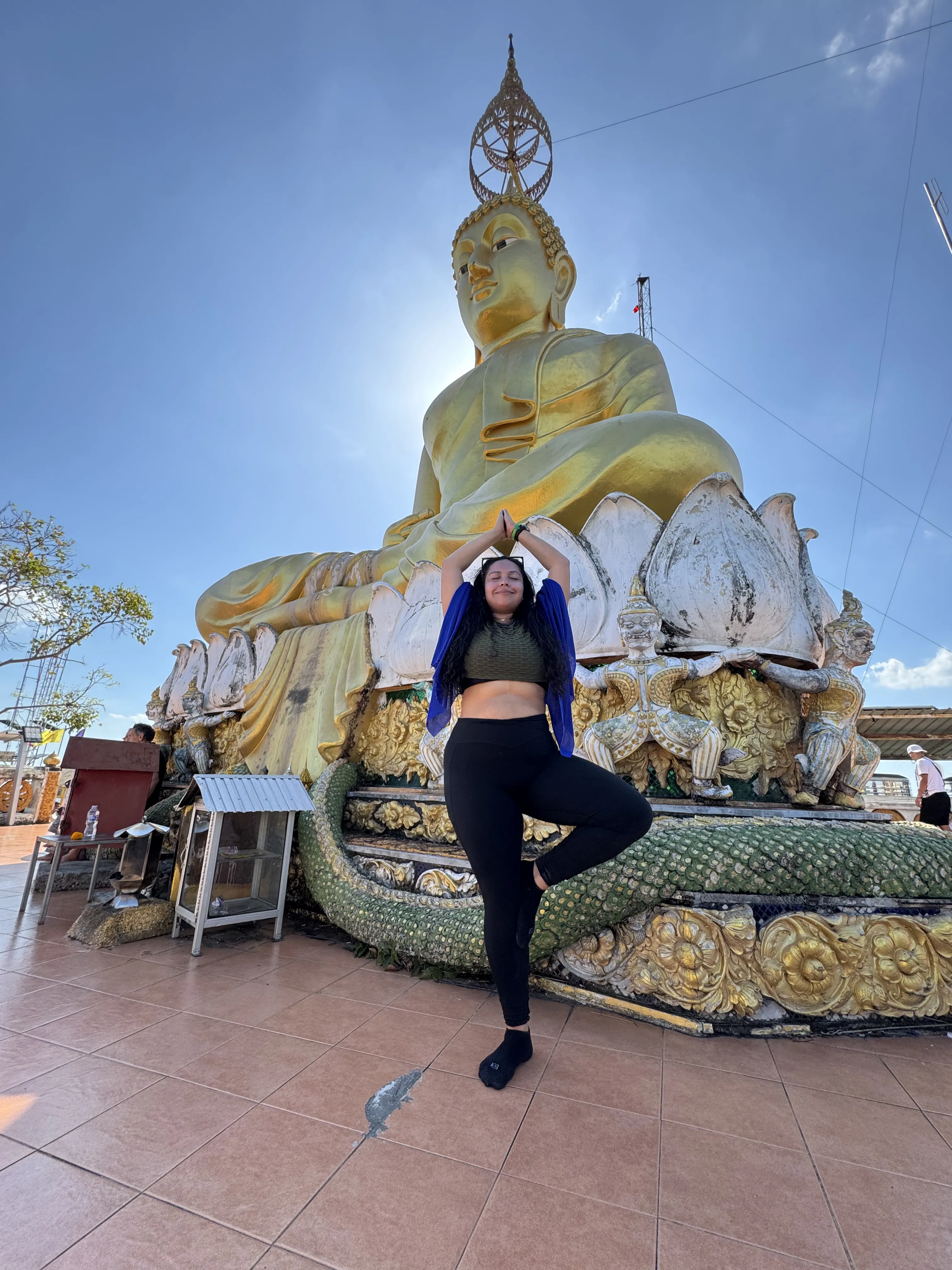 Woman meditating in front of a large golden Buddha statue.