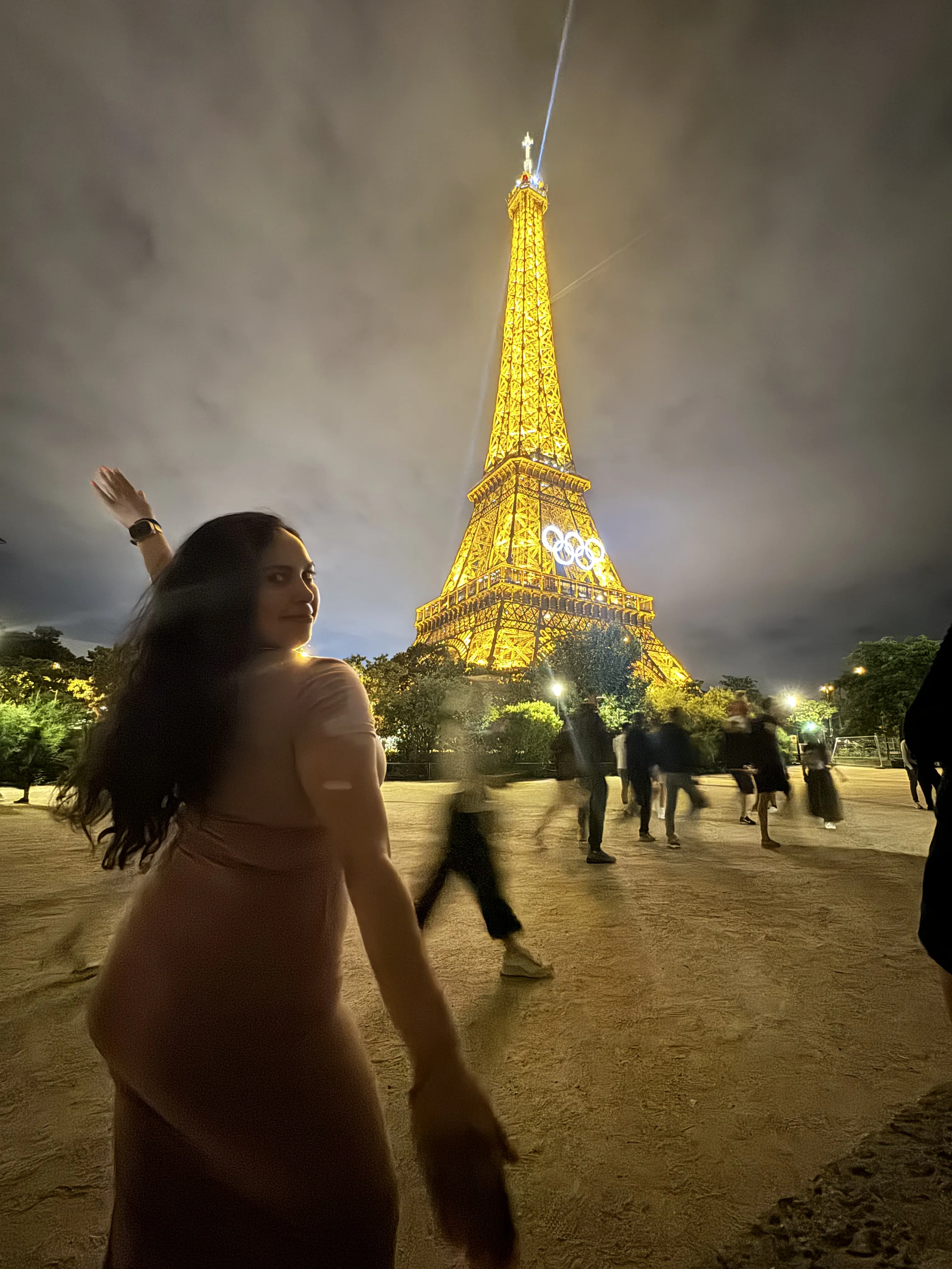 Woman in a pink dress poses joyfully in front of the illuminated Eiffel Tower.