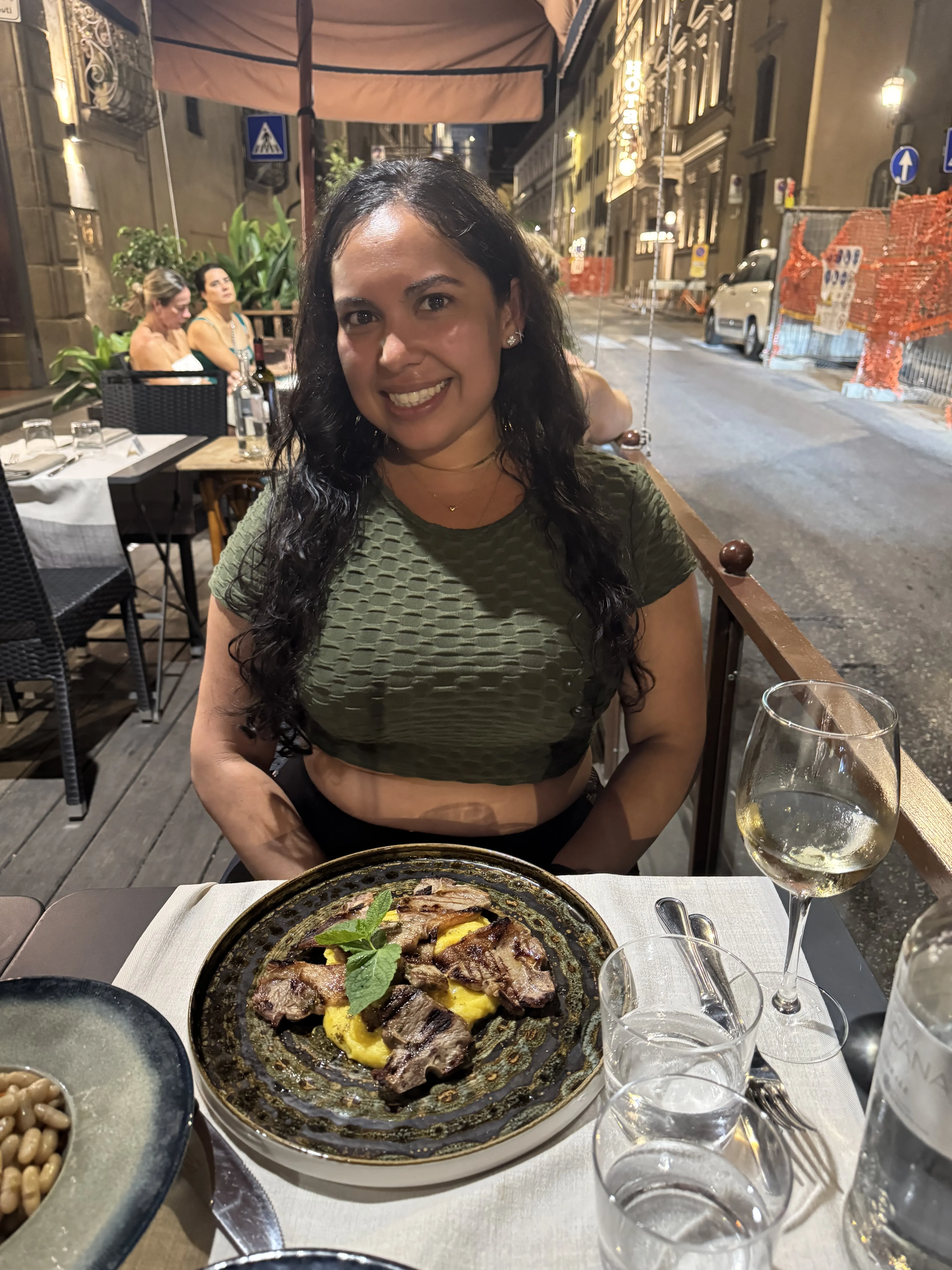 Woman smiling at a restaurant table with a plate of food and wine.